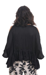 Load image into Gallery viewer, Back top half view of a woman wearing the rhys ruffle blouse in black. This top has a cold shoulder, 3/4 length sleeves, and a ruffled hem. On the bottom the woman is wearing black and white printed pants.
