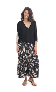 Front full body view of a woman wearing the alembika speckle mandala wide pant and the alembika black multi colorblock top. This top has a beige back, beige right sleeve, beige trim on the left side of the v-neck and a beige back. The front of the top and left sleeve are black. The top has drop shoulder 3/4 length sleeves.