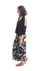 Load image into Gallery viewer, Left side full body view of a woman wearing the alembika speckle mandala wide pant and the alembika black multi colorblock top. This top has a beige back, beige right sleeve, beige trim on the left side of the v-neck and a beige back. The front of the top and left sleeve are black. The top has drop shoulder 3/4 length sleeves.
