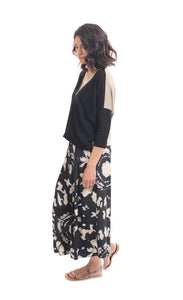 Left side full body view of a woman wearing the alembika speckle mandala wide pant and the alembika black multi colorblock top. This top has a beige back, beige right sleeve, beige trim on the left side of the v-neck and a beige back. The front of the top and left sleeve are black. The top has drop shoulder 3/4 length sleeves.
