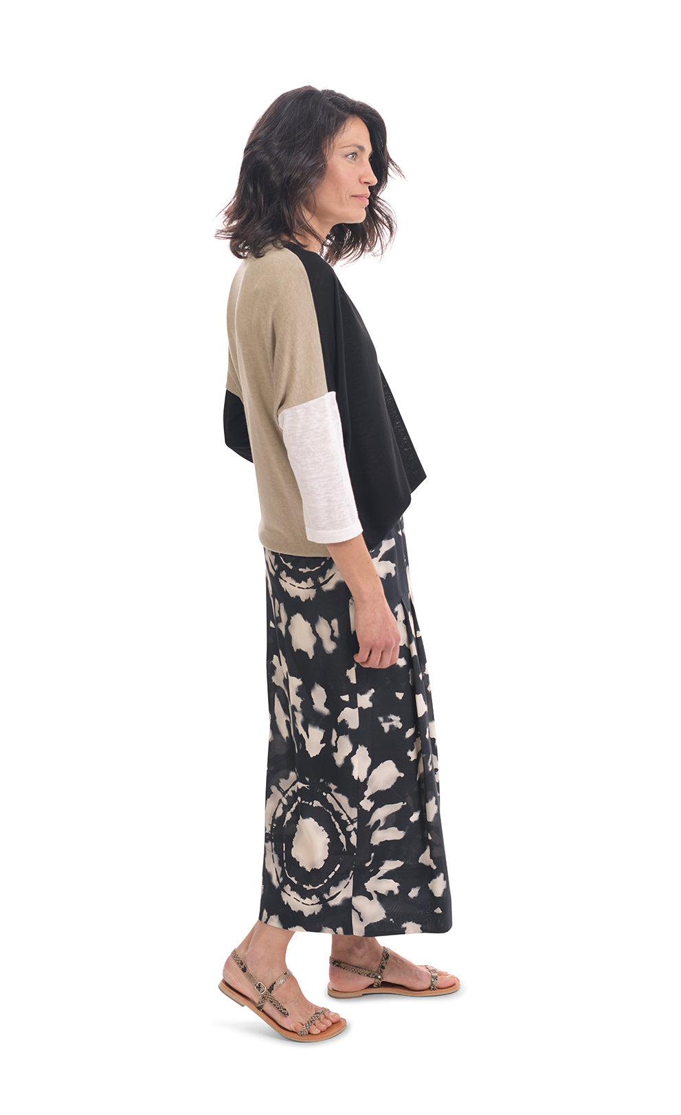 Right side full body view of a woman wearing the alembika speckle mandala wide pant and the alembika black multi colorblock top. This top has a beige back, beige right sleeve, beige trim on the left side of the v-neck and a beige back. The front of the top and left sleeve are black. The top has drop shoulder 3/4 length sleeves.
