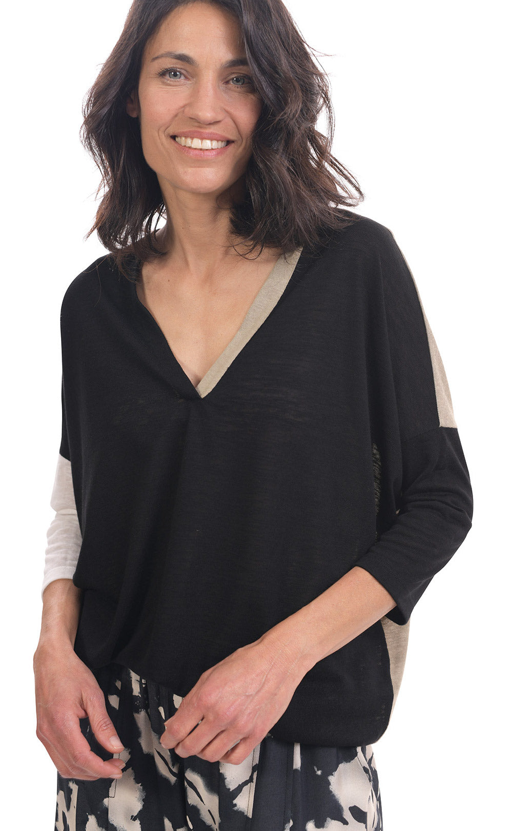 Front top half view of a woman wearing the alembika speckle mandala wide pant and the alembika black multi colorblock top. This top has a beige back, beige right sleeve, beige trim on the left side of the v-neck and a beige back. The front of the top and left sleeve are black. The top has drop shoulder 3/4 length sleeves.