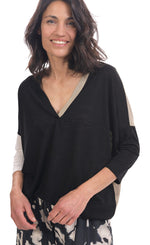 Load image into Gallery viewer, Front top half view of a woman wearing the alembika speckle mandala wide pant and the alembika black multi colorblock top. This top has a beige back, beige right sleeve, beige trim on the left side of the v-neck and a beige back. The front of the top and left sleeve are black. The top has drop shoulder 3/4 length sleeves.
