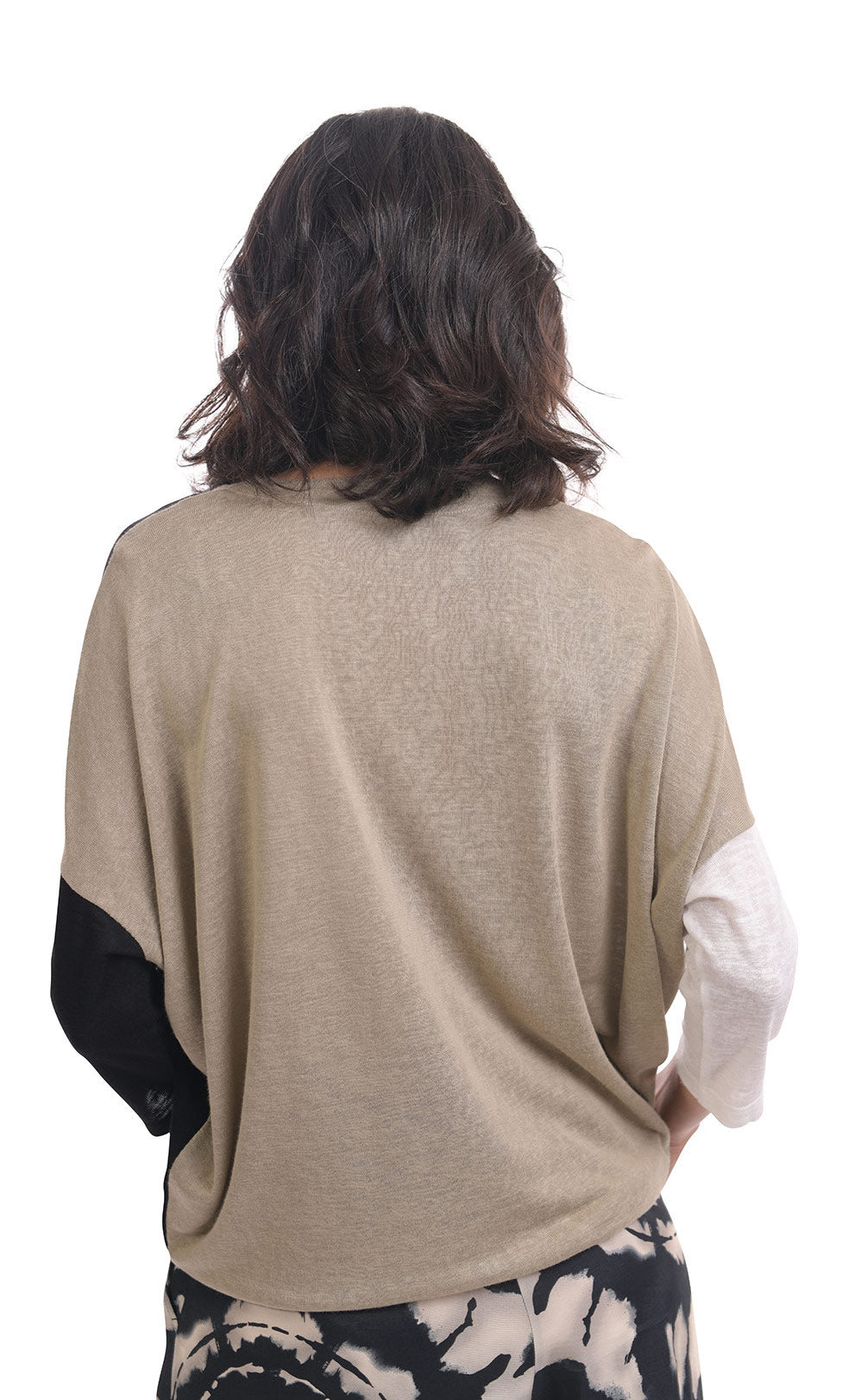 Back top half view of a woman wearing the alembika speckle mandala wide pant and the alembika black multi colorblock top. This top has a beige back, white right sleeve, and black left sleeve. 