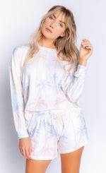 Load image into Gallery viewer, Front top half view of a woman wearing the pj salvage lounge life long sleeve top and the pj salvage lounge life short. The matching top and short are white with a ombre multicolored palm tree print.

