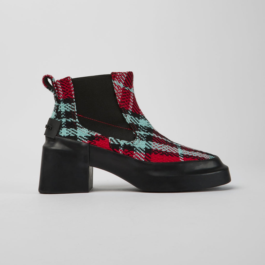 Outer side view of the camper blanket/rain multicolor boot. This boot has a chelsea style with elastic sides. The shoe has a red, black, and blue plaid print and a chunky black heel.