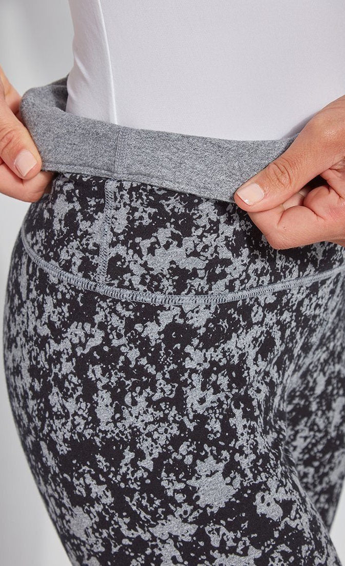 Close up, side view of the waistband of the Lysse Reversible Cotton Legging. The legging has a grey and black speckled print. The woman is folding over the waistband to show the solid grey reversible side.