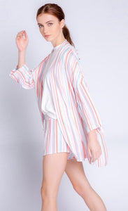 Left side full body view of a woman wearing the pj salvage saturday morning stripe jacket. This jacket has multicolored stripes, a draped open front, and 3/4 length drop shoulder sleeves. on the bottom the model is wearing matching shorts.