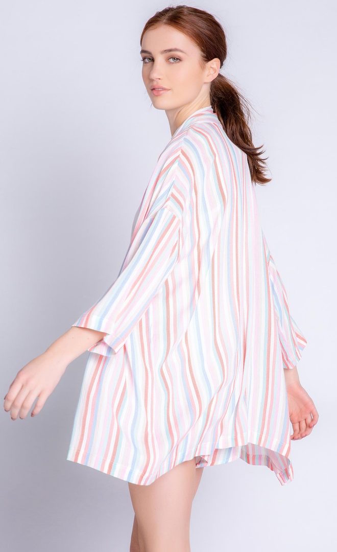 Back left sided full body view of a woman wearing the pj salvage saturday morning stripe jacket. This jacket has multicolored stripes and 3/4 length drop shoulder sleeves. on the bottom the model is wearing matching shorts.