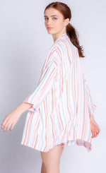 Load image into Gallery viewer, Back left sided full body view of a woman wearing the pj salvage saturday morning stripe jacket. This jacket has multicolored stripes and 3/4 length drop shoulder sleeves. on the bottom the model is wearing matching shorts.
