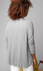 Load image into Gallery viewer, Back, top half view of a woman wearing the grey Lola &amp; Sophie scoop neck shirttail tee. This shirt has a boxy silhouette and fitted sleeves.
