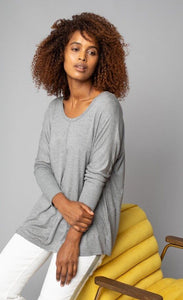 Front, left side, top half view of a woman wearing the grey Lola & Sophie scoop neck shirttail tee. This shirt has a boxy silhouette, indent detailing around the neck and down the front, and fitted sleeves.