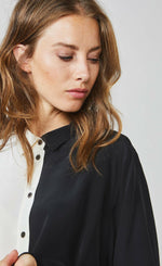 Load image into Gallery viewer, Front close up view of a woman wearing the summum color block blouse. This blouse is black on the left side and ivory on the right side with a button up front.
