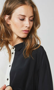 Front close up view of a woman wearing the summum color block blouse. This blouse is black on the left side and ivory on the right side with a button up front.