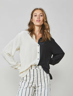 Load image into Gallery viewer, Front top half view of a woman wearing the summum color block blouse. This blouse is black on the left side and ivory on the right side. It has a button up front and long sleeves. On the bottom the model is wearing the summum striped trouser
