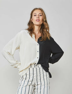 Front top half view of a woman wearing the summum color block blouse. This blouse is black on the left side and ivory on the right side. It has a button up front and long sleeves. On the bottom the model is wearing the summum striped trouser