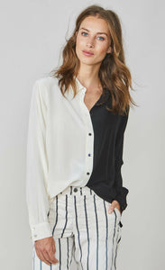 Front top half view of a woman wearing the summum color block blouse. This blouse is black on the left side and ivory on the right side. It has a button up front and long sleeves. On the bottom the model is wearing the summum striped trouser