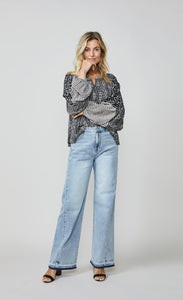 Front full body view of a woman wearing wide leg jeans and the summum kimono printed top. This top is black with a white print. It has an oversized silhouette and long puffy sleeves.