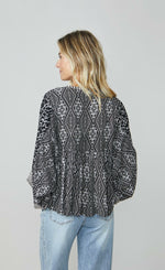 Load image into Gallery viewer, Back top half view of a woman wearing wide leg jeans and the summum kimono printed top. This top is black with a white print. It has an oversized silhouette and long puffy sleeves.
