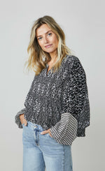 Load image into Gallery viewer, Front top half view of a woman wearing wide leg jeans and the summum kimono printed top. This top is black with a white print. It has an oversized silhouette and long puffy sleeves.

