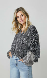 Front top half view of a woman wearing wide leg jeans and the summum kimono printed top. This top is black with a white print. It has an oversized silhouette and long puffy sleeves.