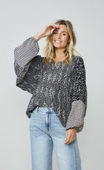 Load image into Gallery viewer, Front top half view of a woman wearing wide leg jeans and the summum kimono printed top. This top is black with a white print. It has an oversized silhouette and long puffy sleeves.
