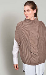 Load image into Gallery viewer, Front top half view of a woman wearing jeans, a white long sleeve shirt, and the summum sleeveless cable knit sweater. This sweater is ribbed with a cable knit band down the middle front. The sweater also has a ribbed stand collar.
