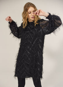 Front full body view of a woman wearing the summum fluffy dress in black. This dress has sparkly fringe on a chevron pattern and ends slightly above the knees.