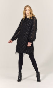 Front full body view of a woman wearing the summum fluffy dress in black. This dress has sparkly fringe on a chevron pattern and ends slightly above the knees.