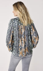 Load image into Gallery viewer, Back top half view of a woman wearing the summum ikat print top. This top is black and white with seafoam green and orange mixed in. The top has prairie long sleeves, and a relaxed fit.

