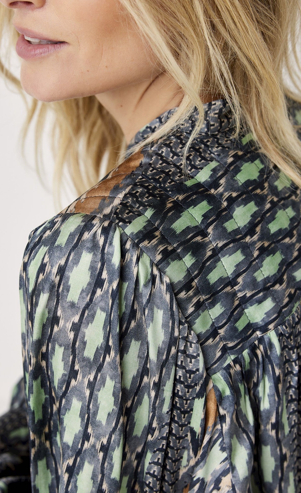 Back close up view of a woman wearing the summum ikat print top. This top is black and white with seafoam green and orange mixed in. The top has prairie long sleeves, a relaxed fit, and a v-neck.