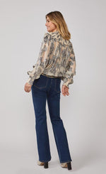 Load image into Gallery viewer, Back full body view of a woman wearing jeans and the summum lurex flower blouse. This blouse is cream/shell colored with metallic flowers all over it, balloon sleeves, and a round shoulder panel with ruffles.

