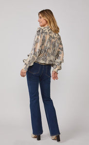 Back full body view of a woman wearing jeans and the summum lurex flower blouse. This blouse is cream/shell colored with metallic flowers all over it, balloon sleeves, and a round shoulder panel with ruffles.