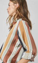 Load image into Gallery viewer, Side close up view of a woman wearing the summum multicolor striped blouse. This blouse has rust, mustard, blue, and green stripes separated by a light blue. The blouse also has a button up front and rolled up long sleeves.
