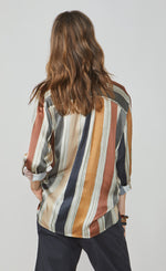 Load image into Gallery viewer, Back top half view of a woman wearing full navy capris and the summum multicolor striped blouse. This blouse has rust, mustard, blue, and green stripes separated by a light blue. The blouse also has a yoked back and rolled up long sleeves.
