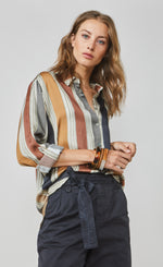Load image into Gallery viewer, Front top half view of a woman wearing full navy capris and the summum multicolor striped blouse. This blouse has rust, mustard, blue, and green stripes separated by a light blue. The blouse also has a button up front and rolled up long sleeves.
