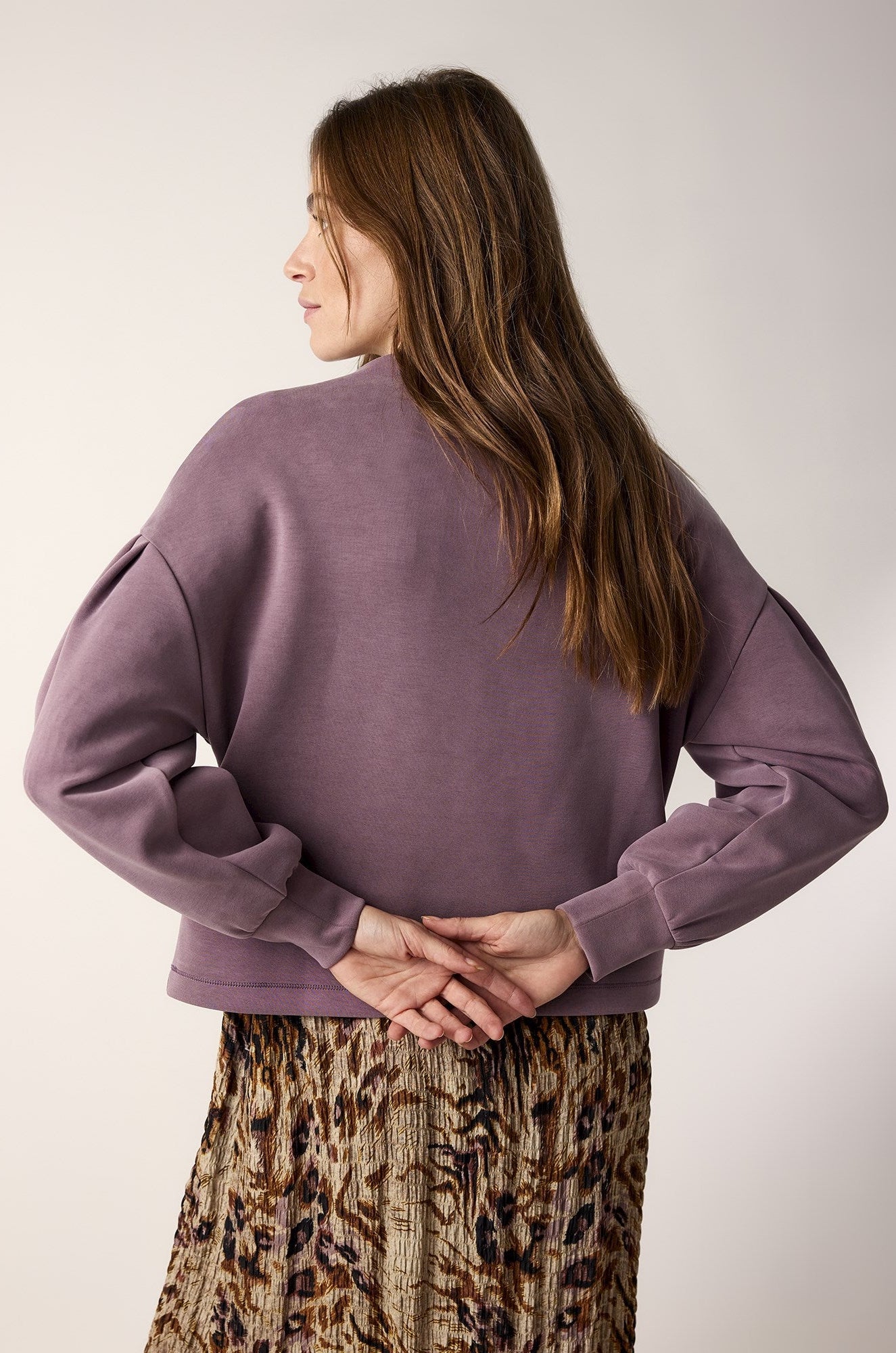 Back top half view of a woman wearing the summum scuba pullover. This pullover is mauve colored, has drop shoulders, long puff sleeves, and cuffs. The top also has a boat neck.