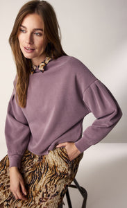 Front top half view of a woman wearing the summum scuba pullover. This pullover is mauve colored, has drop shoulders, long puff sleeves, and cuffs. The top also has a boat neck.