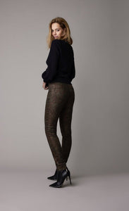 Back full body view of a woman wearing a black top and the summum Skinny trousers with foil print. This pant is caramel bronze colored with a small metallic gold and brown leaf print all over it.