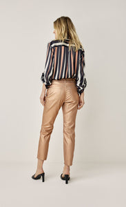 Back full body view of a woman wearing a black, pink, and white striped shirt and the summum skinny foil coated trousers. These trousers are rose gold colored.