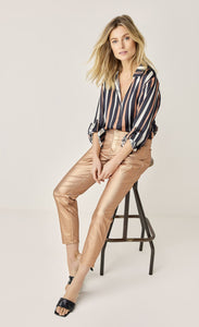 Front full body view of a woman wearing a black, pink, and white striped shirt and the summum skinny foil coated trousers. These trousers are rose gold colored.