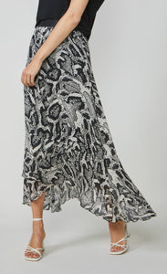 Front bottom half view of a woman wearing the summum printed maxi skirt. This skirt has a black and white snake skin print with a black waistband. The skirt has an asymmetrical hem and a flowy look.