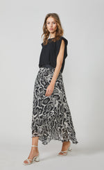 Load image into Gallery viewer, Front full body view of a woman wearing the summum black shoulder pad top and the summum printed maxi skirt. This skirt has a black and white snake skin print with a black waistband. The skirt has an asymmetrical hem and a flowy look.
