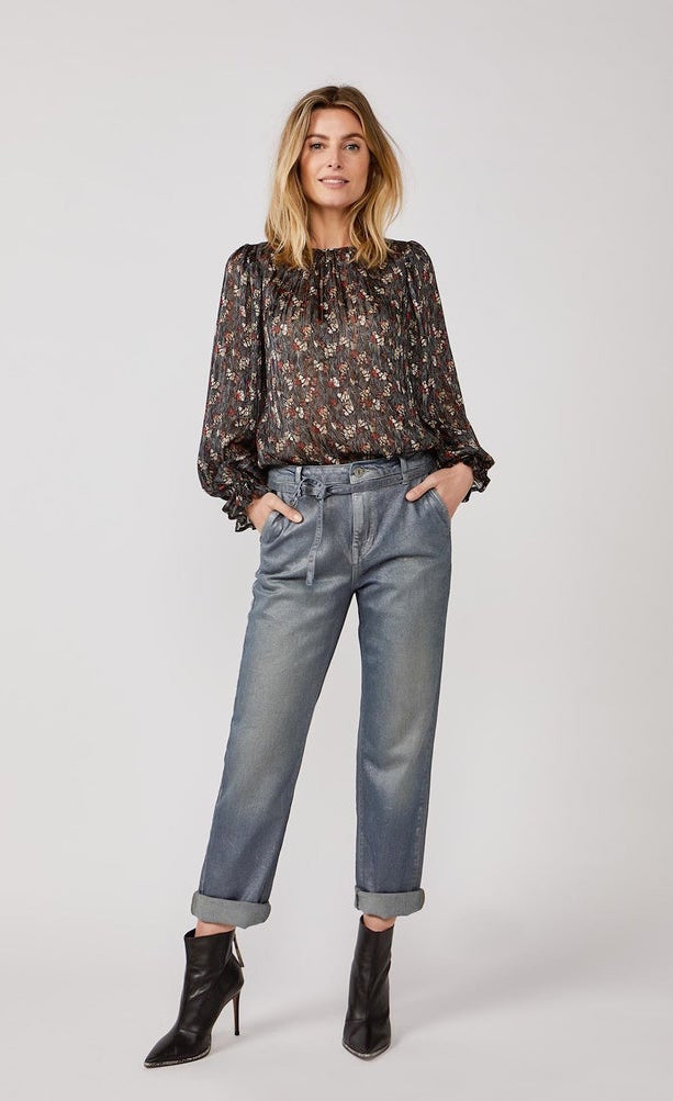 Front full body view of a woman wearing a black top with print and the summum straight blue daze denim pants. These jeans are blue-grey with a shimmer. They have a cropped and cuffed bottom, pockets, and a tie belt.