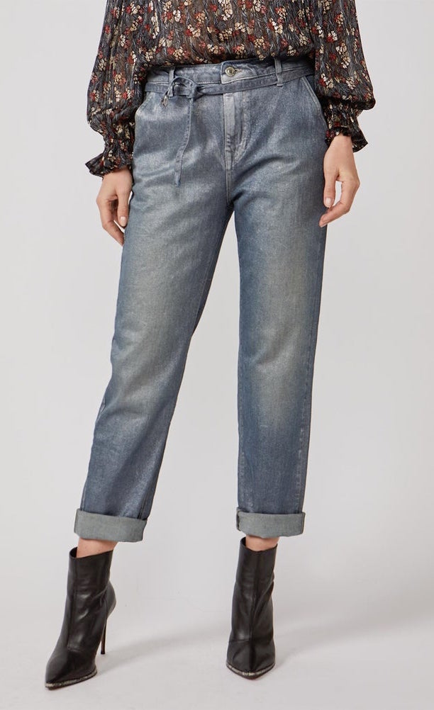 Front bottom half view of a woman wearing a black top with print and the summum straight blue daze denim pants. These jeans are blue-grey with a shimmer. They have a cropped and cuffed bottom, pockets, and a tie belt.