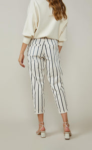 Back bottom half view of a woman wearing a white top and the summum striped cotton trouser. This pant is ivory colored with black stripes. It is wider around the hips and tapers in above the ankles where it ends.  The back has slit pockets.