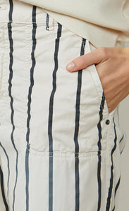 Front close up view of a woman wearing the summum striped cotton trouser. This pant is ivory colored with black stripes. This image shows off the side pocket.