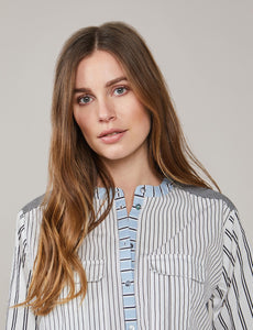 Front top half close up view of a woman wearing the summum mixed stripes blouse. This blouse has a button down front and two breast pockets. The shirt has different black stripes on a white background with hints of blue.