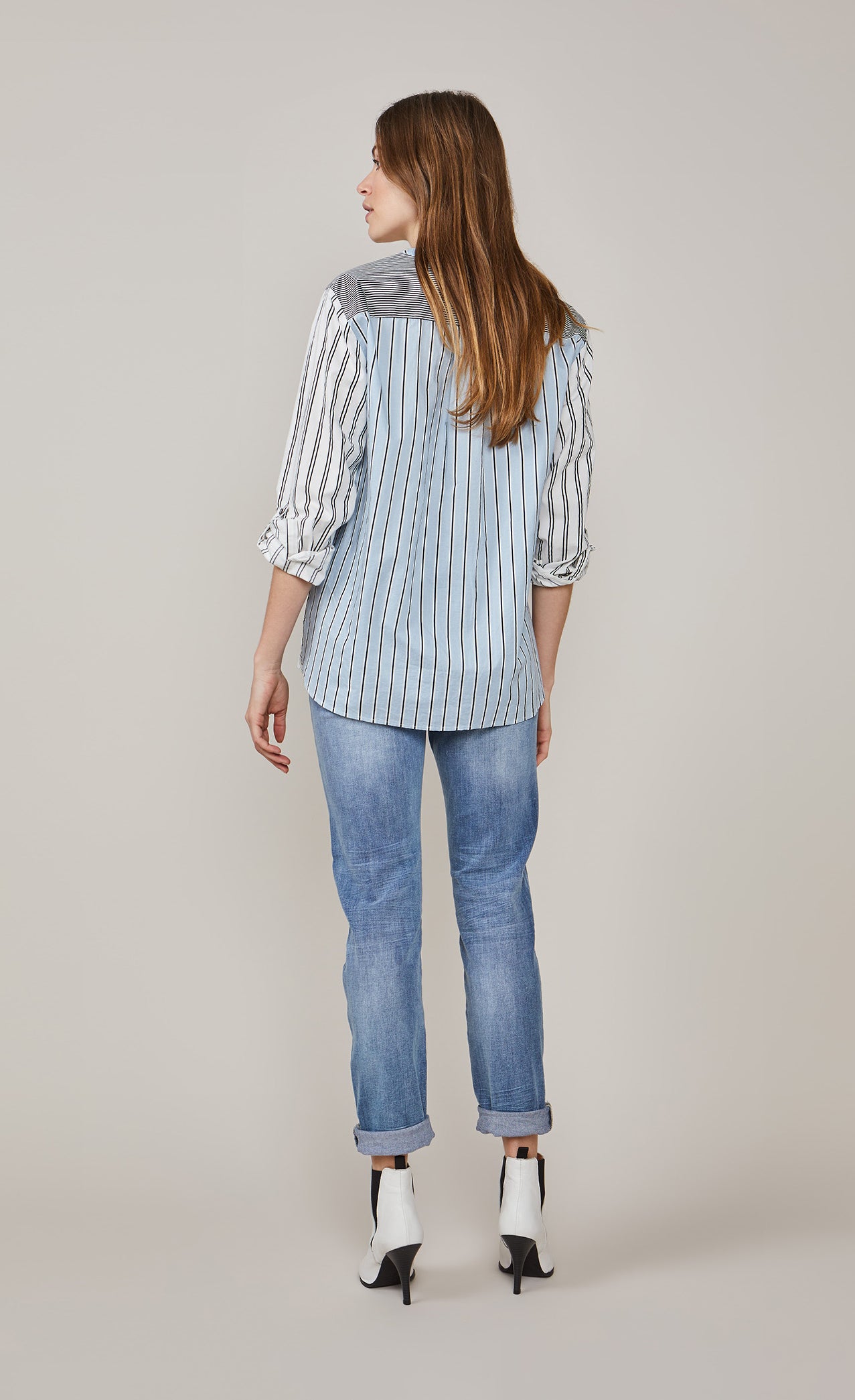 Back full body view of a woman wearing the summum mixed stripes blouse. This blouse rolled up sleeves, a yoked back, black stripes on a blue and white background.