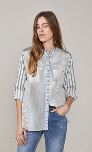 Front top half view of a woman wearing the summum mixed stripes blouse. This blouse has a button down front, rolled up sleeves, and two breast pockets. The shirt has different black stripes on a white background with hints of blue.